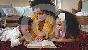 African American mother with her cute children lying on floor and reading a book