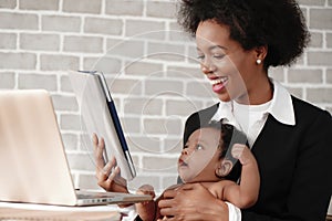 African american mother holding her baby boy on hands while working with laptop computer at home