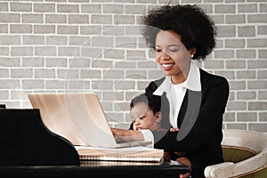 African american mother holding her baby boy on hands while working with laptop computer at home