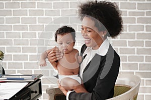 African american mother holding her baby boy on hands while working with laptop computer at home