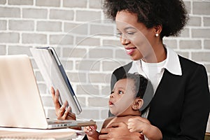 African american mother holding her baby boy on hands while working with laptop computer at home