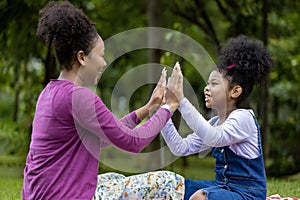 African American mother is laughing while playing patty cake with her young daughter while having a summer picnic in the public