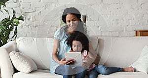 African American mother little daughter hug play game on touchpad