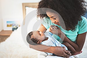 African American mother looking and holding hand, her 1-month-old baby newborn son lying in bed