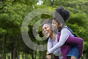 African American mother is playing piggyback riding with her young daughter while having a summer picnic in the public park for