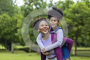 African American mother is playing piggyback riding with her young daughter while having a summer picnic in the public park for