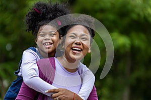 African American mother is playing piggyback riding with her young daughter while having a summer picnic in the public park for