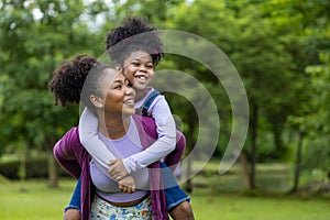 African American mother is playing piggyback riding with her young daughter while having a summer picnic in the public park for