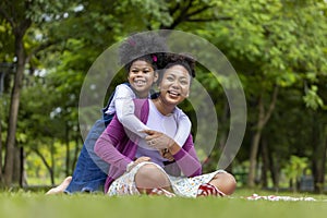 African American mother is playing piggyback riding and hugging with her young daughter while having a summer picnic in the public