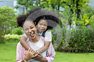 African American mother is playing piggyback riding and hugging with her young daughter while having a summer picnic in the public