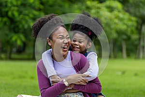 African American mother is playing piggyback riding and hugging with her young daughter while having a summer picnic in the public