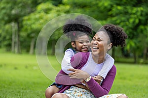 African American mother is playing piggyback riding and hugging with her young daughter while having a summer picnic in public