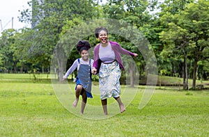 African American mother running barefoot on the grass lawn with her young daughter while having a summer picnic in the public park