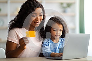 African American mother shopping online with credit card, making purchases on internet with her daughter from home