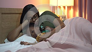 African american mother singing lullaby for little daughter before going to Sleep on bed at home. black mom story telling to girl
