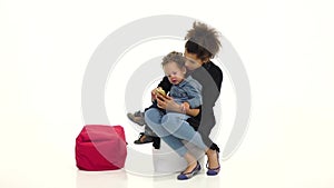 African american mother is sitting with her baby, holding a phone. White background. Slow motion