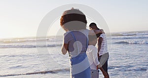 African american mother and son dancing together during sunset at the beach