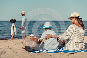 african american mother and son sitting on sand while father and daughter playing