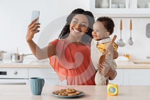 African American Mother Taking Selfie With Little Baby On Smartphone In Kitchen