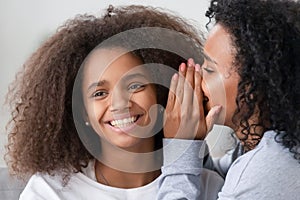 African American mother whispering to smiling teen daughter ear