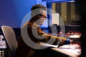 African american music producer operates audio console with moving faders