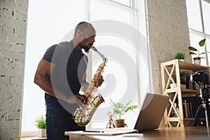 African-american musician playing saxophone during online concert at home isolated and quarantined photo