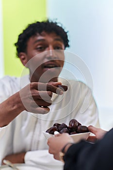 African American Muslim man delicately takes dates to break his fast during the Ramadan month, seated at the family