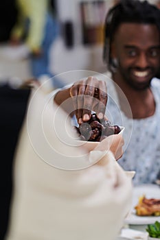 African American Muslim man delicately takes dates to break his fast during the Ramadan month, seated at the family