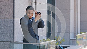 African American office worker man businessman standing on balcony holding smartphone looking in mobile screen