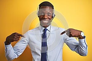 African american operator man working using headset over  yellow background looking confident with smile on face, pointing