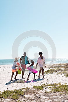 African american parents with children walking on sandy beach against clear sky, copy space