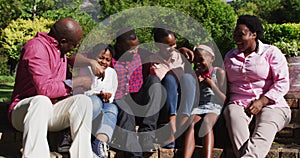 African american parents, grandparents and grandchildren sitting in garden