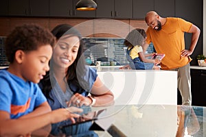 African American Parents Helping Children Studying Homework On Digital Tablets In Kitchen