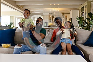African american parents holding children and screaming cheerfully while watching game at home