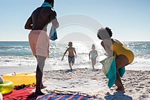 African american parents looking at children racing towards them at beach on sunny day