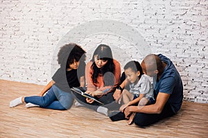 African American parents reading a fairy tale fable story for kids at home. Happy family sitting on the floor indoors.