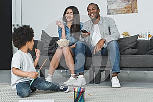 african american parents watching tv and son playing on floor