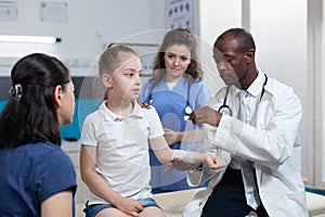 African american pediatrician doctor bandage broken bone of young child arm