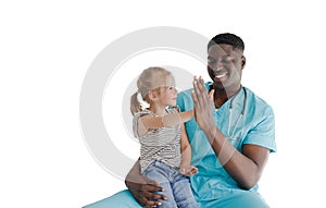 An African-American pediatrician holds a little happy girl patient on his lap, laughing and clapping his hands together