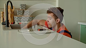 African American plumber repairing sink drain and water supply in kitchen