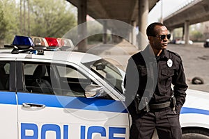 african american police officer leaning back on car