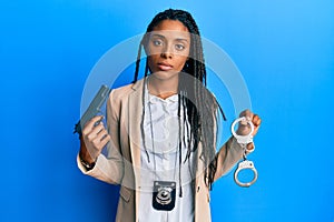 African american police woman holding gun and handcuffs relaxed with serious expression on face