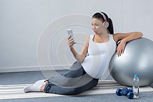 african american pregnant woman listening music with headphones and smartphone while sitting with fit ball