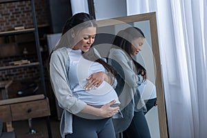 african american pregnant woman looking at her belly while standing