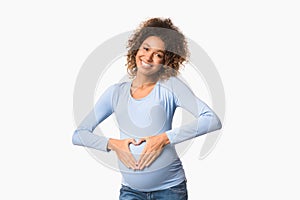 African-american pregnant woman making heart sign on her belly