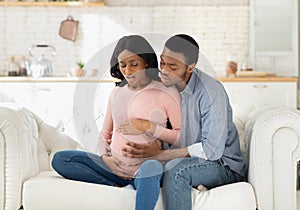 African American pregnant woman suffering from pain, having birth contractions while worried husband helping her at home
