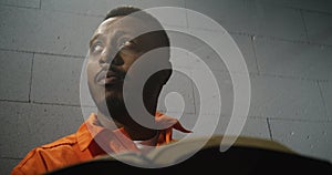 African American prisoner in orange uniform reads Bible