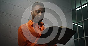 African American prisoner in orange uniform reads Bible