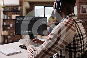 African american programmer with wireless headphones listening to music while writing code