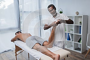 african american rehabilitologist massaging foot of